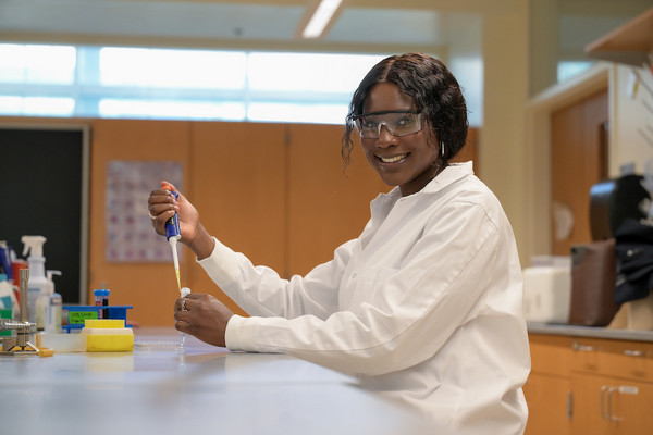 UNF student Isabella Panya in a lab coat and goggles holding lab tools