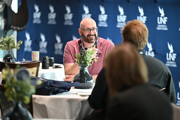 Man sitting at a table smiling while conversing with another gentleman