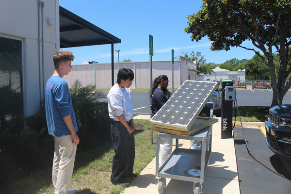 UNF students standing next to a solar panel in a parking lot