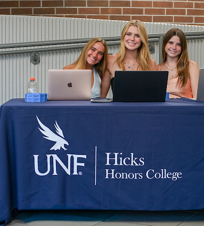 UNF students seated at a table with a Hicks Honors College cover