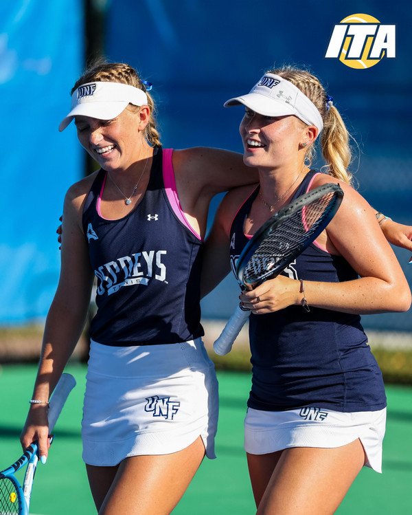 Two members of the UNF Women's Tennis team smiling together on the court
