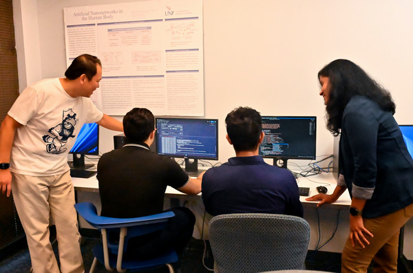 Two UNF students sitting at desktop computers receiving instruction from two UNF faculty members