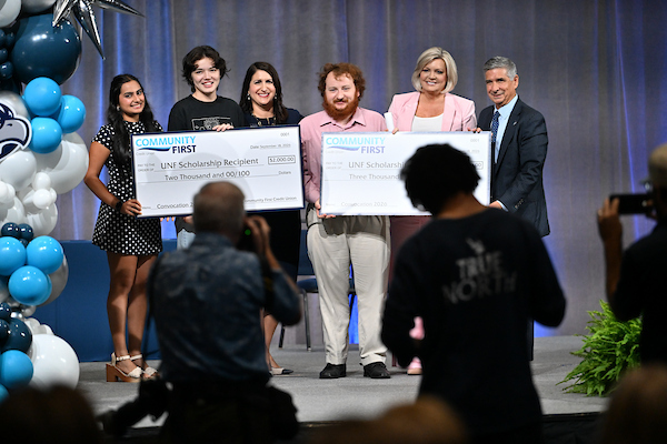 UNF students on stage holding scholarship awards at UNF Convocation 2026