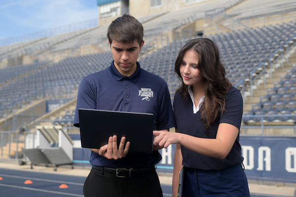 Two UNF students viewing a laptop on the Hodges Stadium track