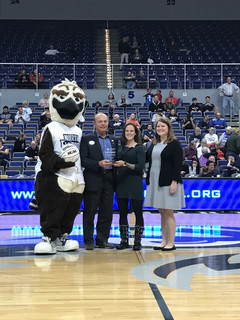 Betty standing at half court in the arena with ozzy the osprey and two others