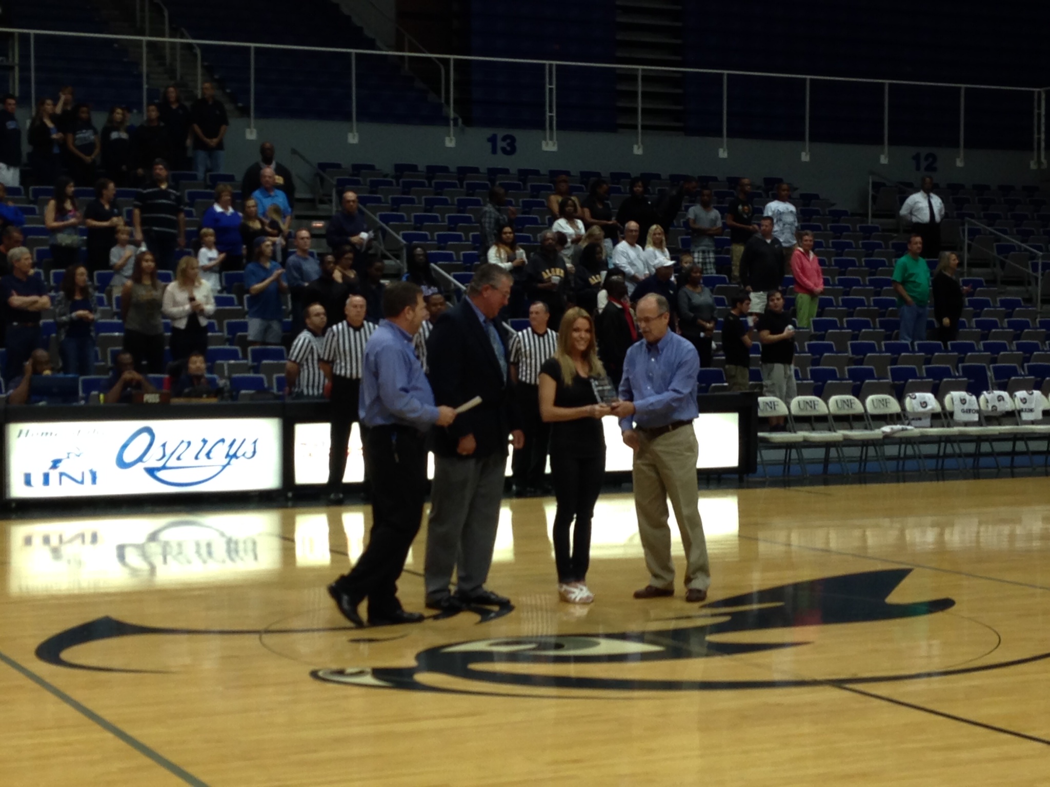 A group of people present Jaime with an award at half court in the arena
