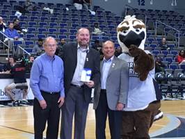Jeremy standing at half court in the arena with ozzy the osprey and two others
