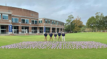 Four students standing in front of the Week of Valor flag display on the UNF Green