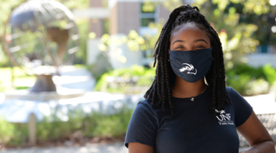 Public health student wearing a dark blue UNF face mask with greenery in the background