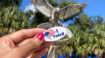 Voting sticker held in front of Osprey fountain on UNF campus