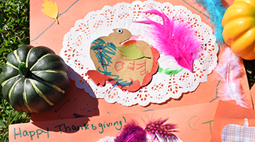 Thanksgiving-themed placemat featuring a cutout of a turkey, green feathers, glitter, and more