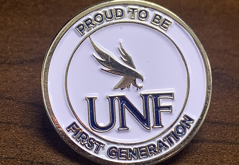Enamel pin with the UNF logo that says “proud to be first generation” 