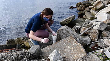 Female student wearing a mask while cleaning up plastics bottles at a cove near the beach