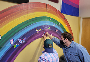 Students in the LGBTQ Center placing hand drawn and designed paper butterflies on a rainbow