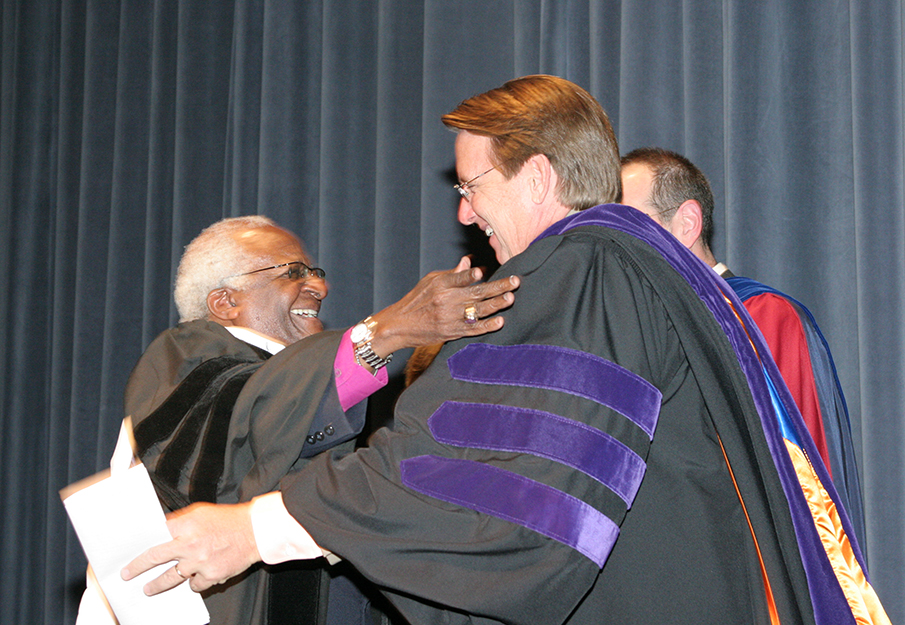 Archbishop Desmond M. Tutu and former UNF president John Delaney embracing on stage at a graduation ceremony
