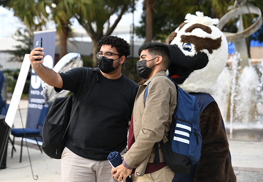 Two male students taking a selfie with Ozzy outside the UNF Arena