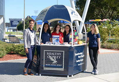 Four students standing next to a Healthy Osprey booth in the Student Union