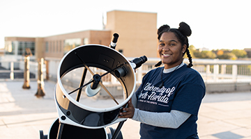 Kennedi Light, UNF student, standing and smiling next to a large outdoor telescope