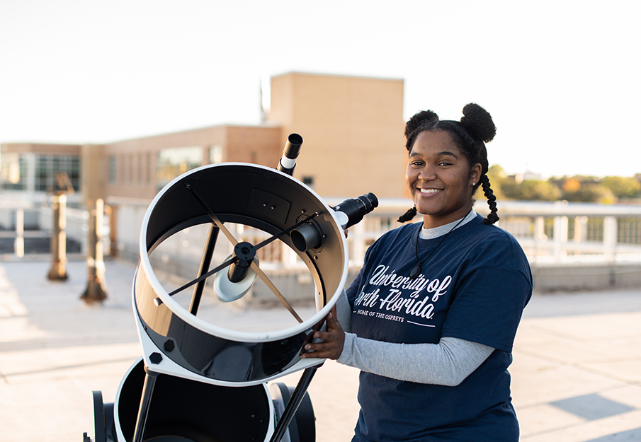 Kennedi Light, UNF student, standing and smiling next to a large outdoor telescope