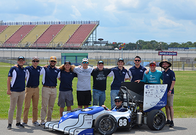 UNF Osprey Racing team at a speedway standing next to their race car
