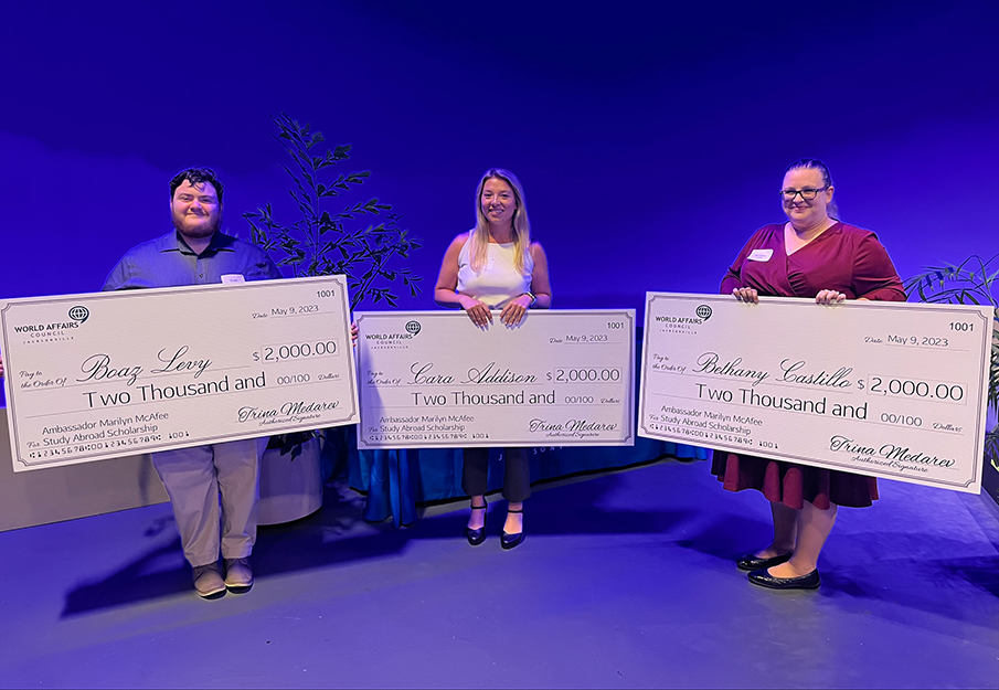 Ambassador Marilyn McAfee Scholarship recipients Boaz Levy, Cara Addison, and Bethany Castillo standing with giant checks