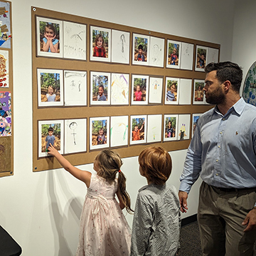 Two UNF preschool students showing their father their displayed art