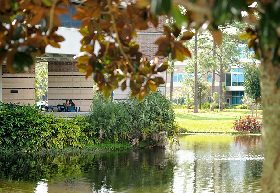 Lake view of Coggin College of Business building, two students studying at table