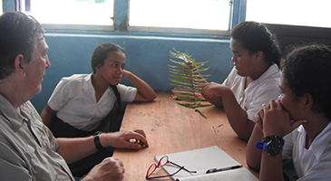 Dr. Cavanaugh sitting with three students from Tuvalu, using accessible resources to teach science