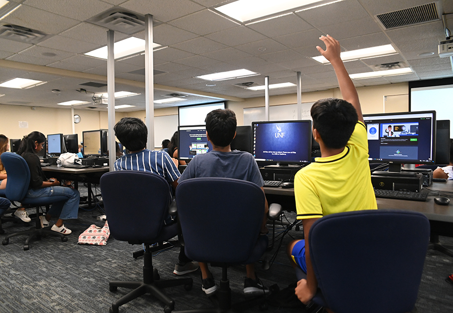 Students sitting in front of computers and one is raising their hand
