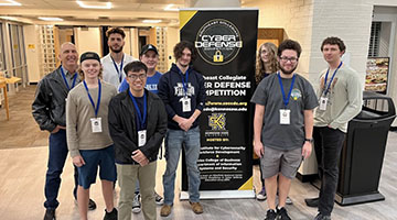 The Osprey Security student team posing in front of a Cyber Defense Competition banner