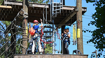 An Eco Adventure volunteer helping put gear onto a student to use the zipline