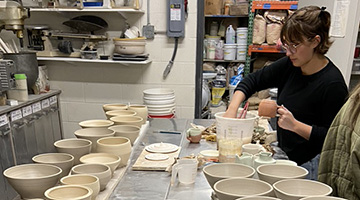 A student dips her hand in a bowl of water while helping create one-of-a-kind bowls