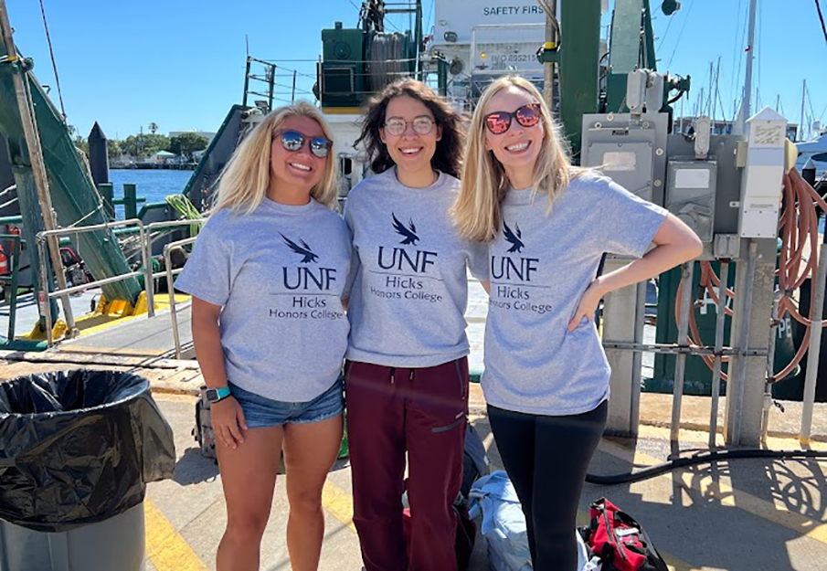2 UNF students and Professor Ziegler posing on a boat wearing UNF t-shirts