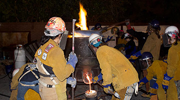 Sculpture students pouring iron into a mold