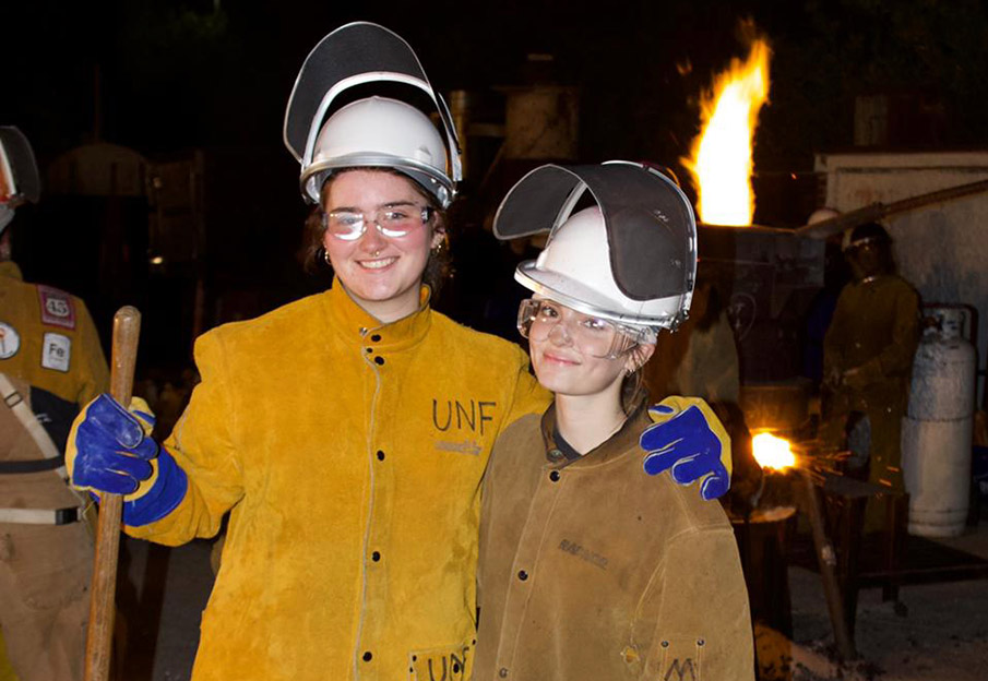 Two UNF sculpture students posing together in front of the iron pour