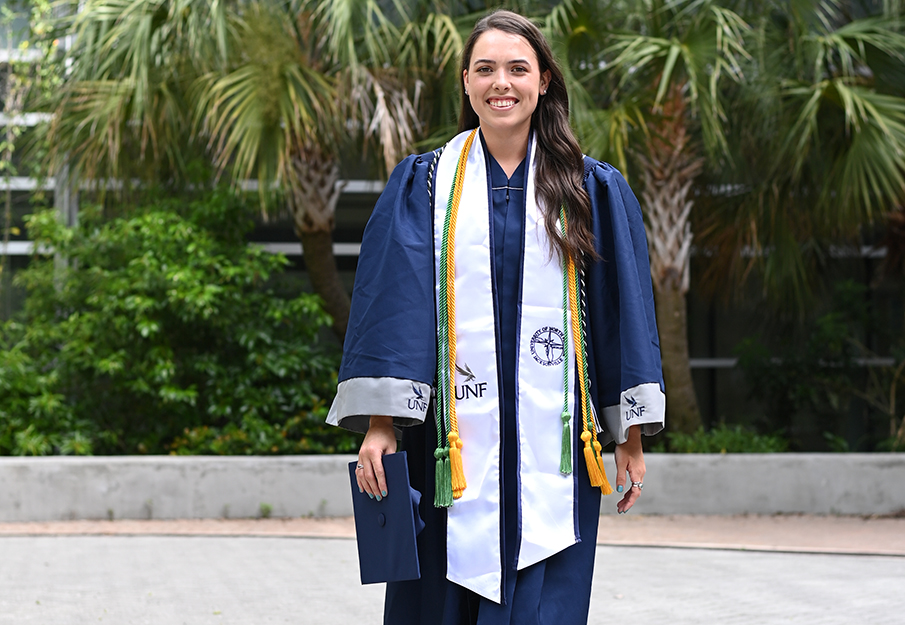 Ashlynn Kemp walking with her cap and gown in front of the biology building