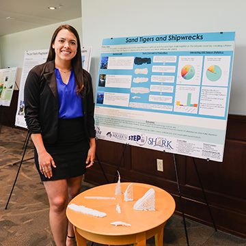 Ashlynn Kemp standing next to her 'Sand Tigers and Shipwrecks' poster