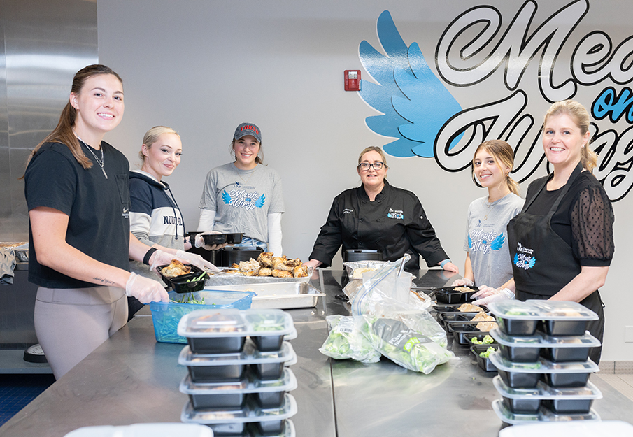 Meals on Wings team posing in front of a table stacked with meals