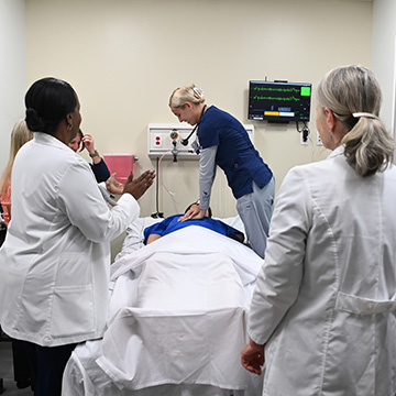 Nursing student practicing CPR on a dummy patient while professors instruct
