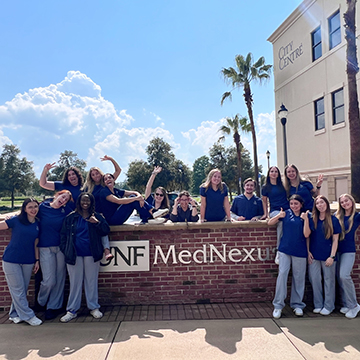 Mia Scarcella and members of the Palm Coast Cohort standing next to a UNF MedNexus sign