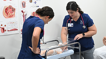 Nursing student observes professor demonstrate a wellness check on an infant dummy