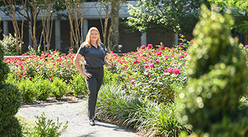 Rhonda Gracie standing next to a bush of blooming roses