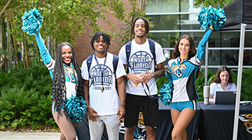 Two students with two Jacksonville Jaguars cheerleaders near the Jaguars season ticket sale booth