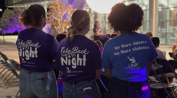 Backs of three students with shirts saying 'Take Back the Night' and 'No More Silence, No More Violence'