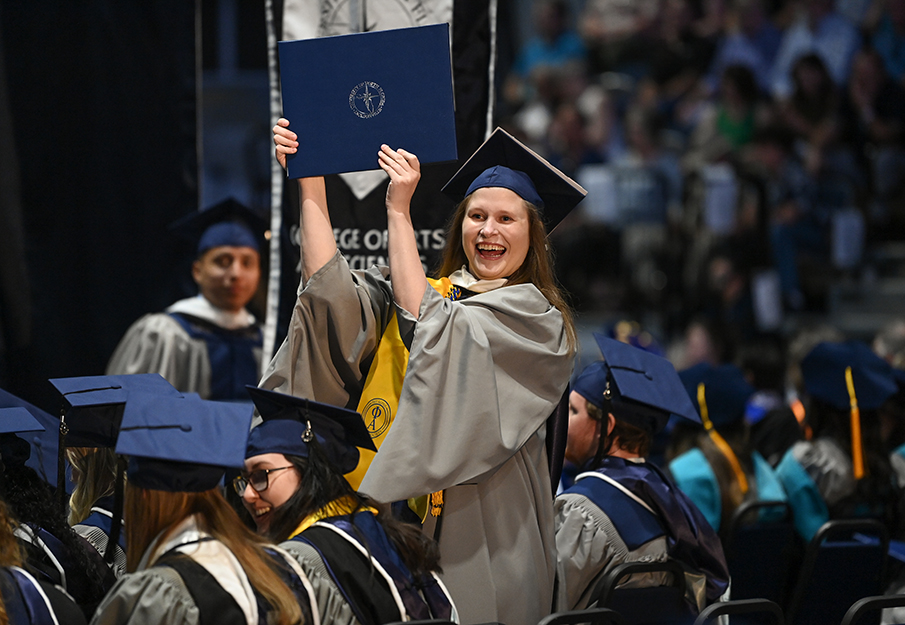 UNF grad smiling wide while holding up her diploma