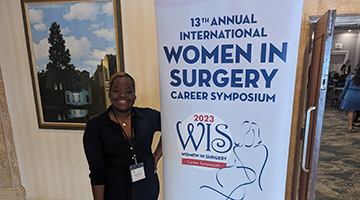 One of the Hicks Honors students standing in front of a sign that reads: "13th Annual International Women in Surgery"