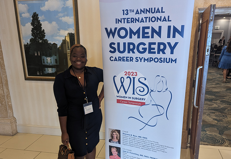 One of the Hicks Honors students standing in front of a sign that reads: "13th Annual International Women in Surgery"