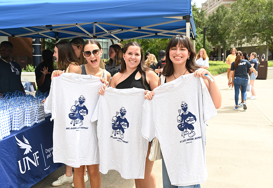 Three new Osprey students holding up t-shirts with Ozzie on them