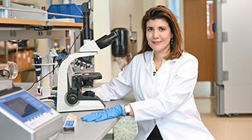 Alya Limayem posed next to a microscope in her white coat