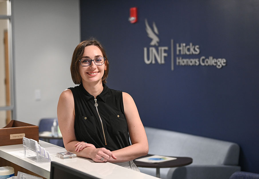 Anna Salvaggio standing behind a desk with a "UNF Hicks Honors College" sign behind her